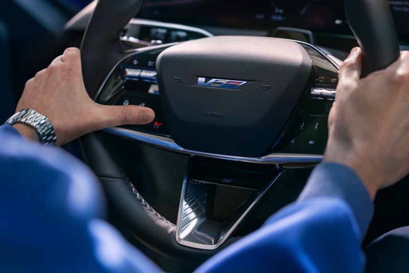 Close-up of a Man About to Press the V-Button on the 2026 OPTIQ-V Steering Wheel | Cadillac of Norwood in Norwood MA